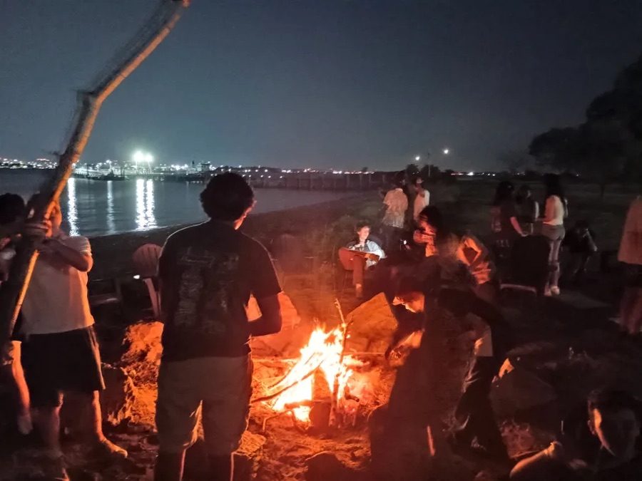 Teenagers around a campfire by the water at night