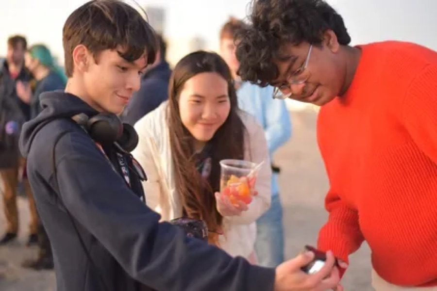 Three teenagers smiling at a gadget one of them built